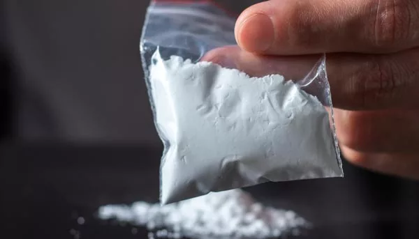 Concept Drug Addiction - Man hand holds plastic packet with cocaine