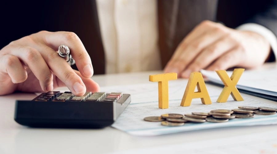 Image of a man's hand on a calculator with the word TAX next to it - Is Rehab Tax Deductible