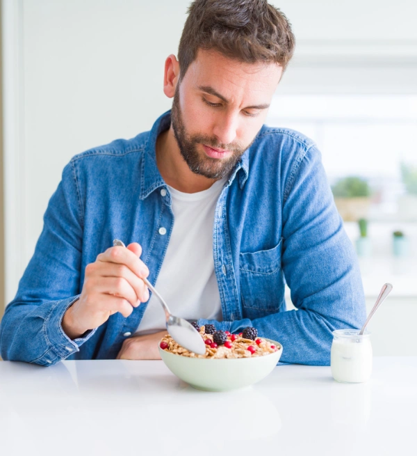 Image of a man sitting at a table eating cereal with a jar of yogurt beside him - Role of a Healthy Diet During Drug or Alcohol Detox