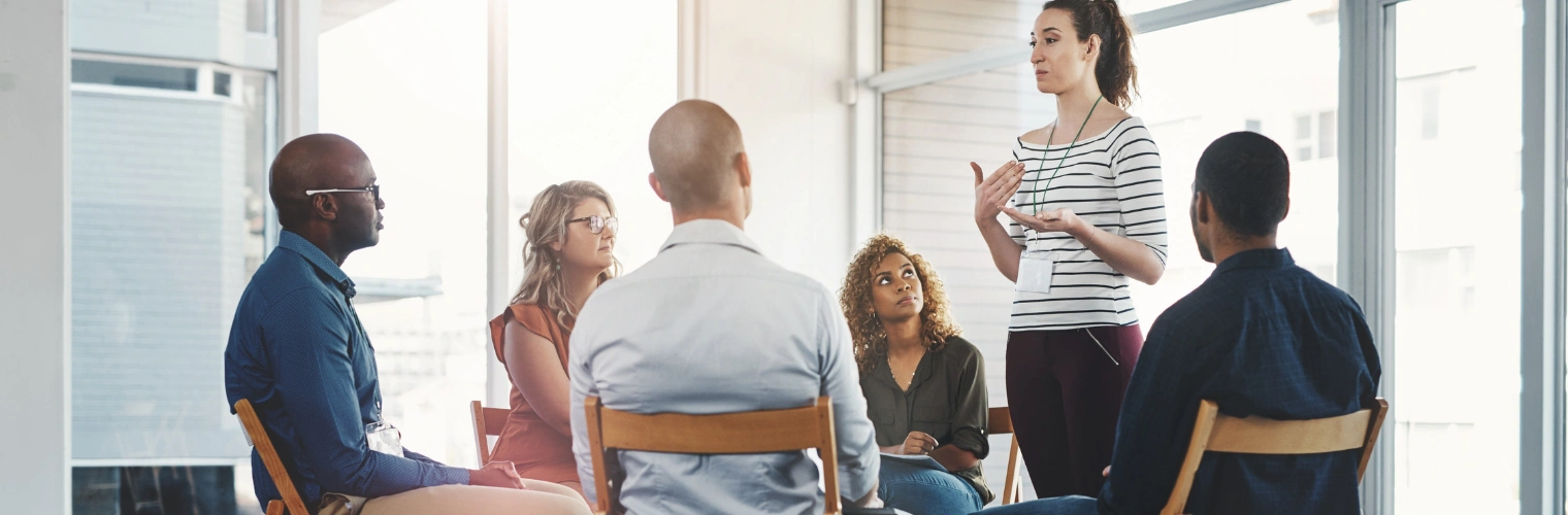 Image of a woman standing up and sharing at an AA meeting as others look on - AA Discussion Meetings and the Power of Sharing
