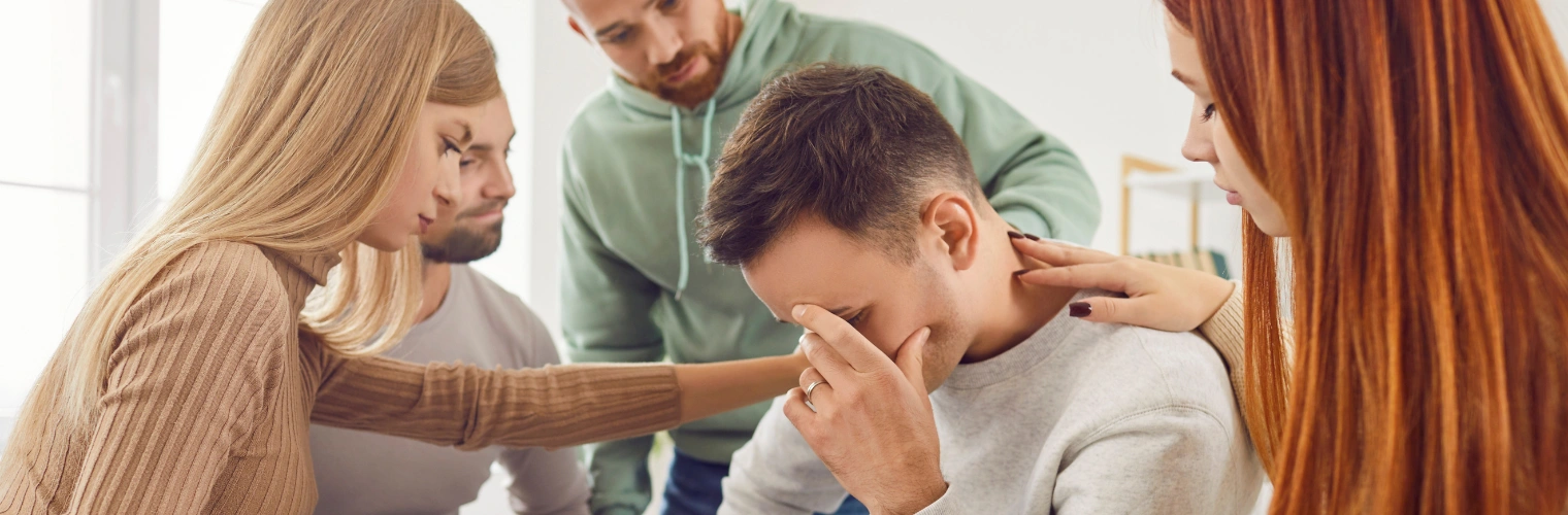 AA meeting participant sitting with hands over face as other group members console him