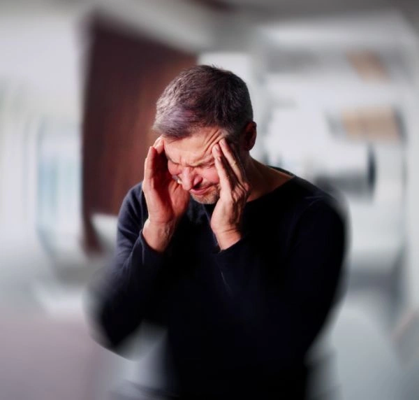 Image of a man standing in a rooom with his hands on his upper forehead experiencing dizziness - Effects of Mixing Benzodiazepine Drugs and Alcohol