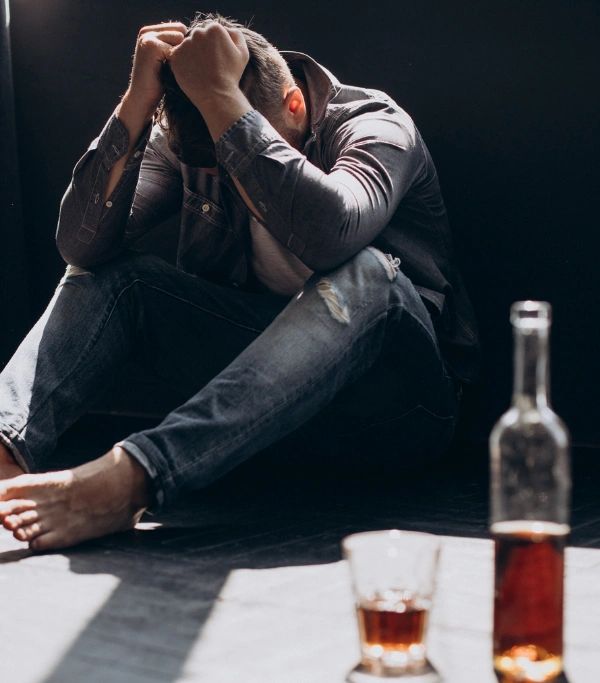 Factors that trigger alcohol cravings Man sitting on the floor with hands over his head with a half glass and bottle of liquor beside him - Factors that trigger alcohol cravings