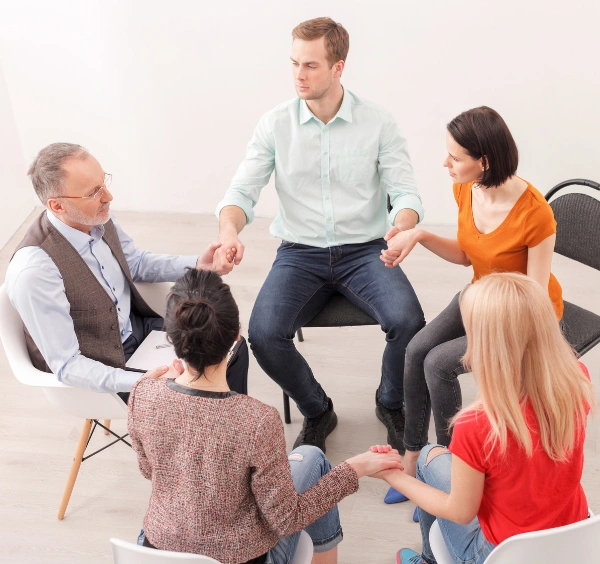 Group of men and women sitting in a circle and holding hands at an NA meeting