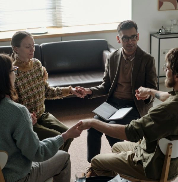 Group of men and women sitting in circle and holding hands at an AA meeting