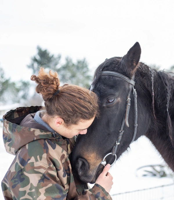 Image of a male wearing a camo jacket standing with his face next to a horse's face - Therapeutic Bond Between Veteran and Horse