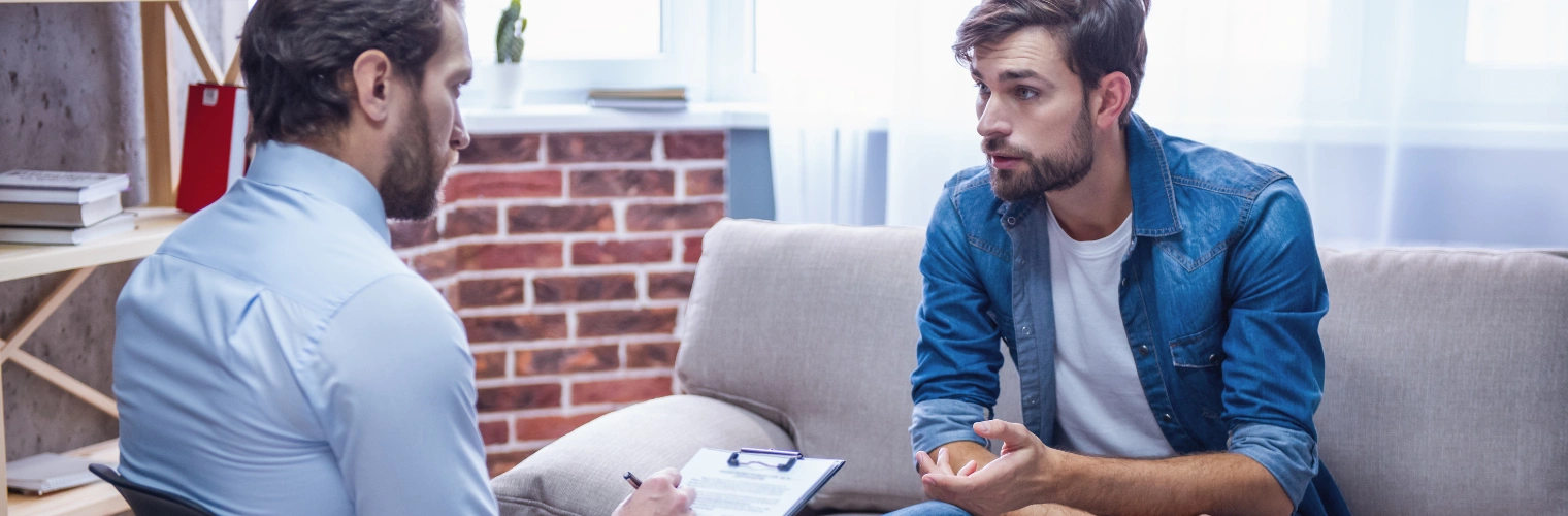 Therapist preparing treatment plan to reduce alcohol cravings Image of a man sitting in a therapy session beside a male counselor taking notes