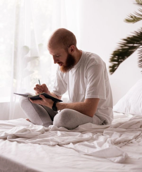 Man sitting on a bed writing his personal inventory