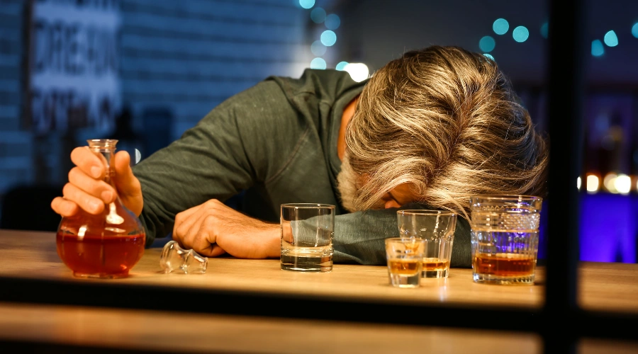 Image of a man surrounded by empty alcohol glasses, illustrating binge drinking