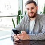 Image of a man sitting with this phone at a rebab center - Can You Have Your Phone in Rehab - Ingrained Recovery