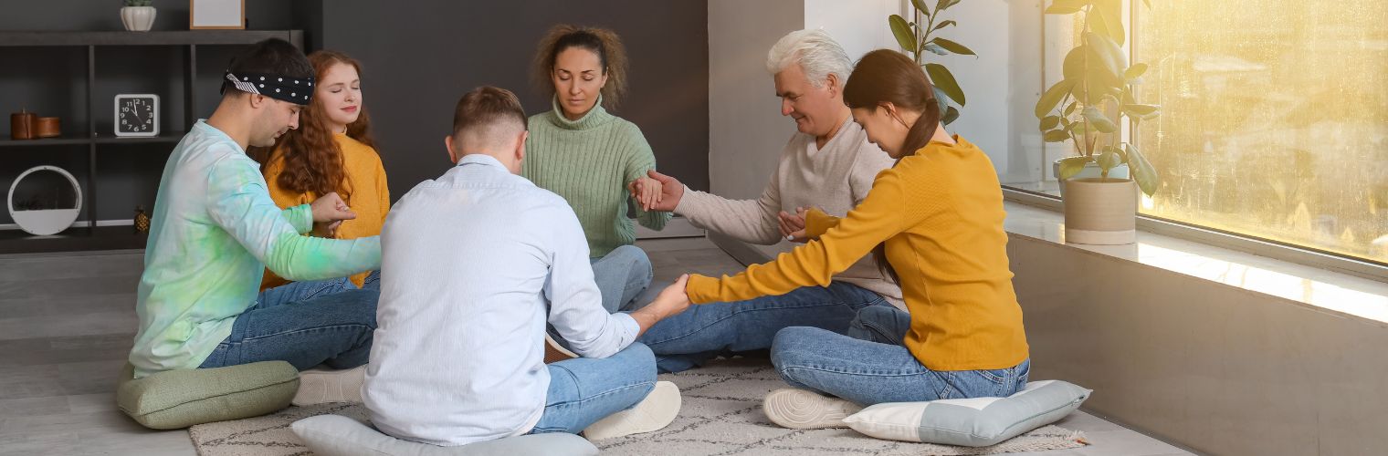 Image of men and women sitting on floor in silent prayer with hands joined at an AA meeting Image of men and women sitting on floor in silent prayer with hands joined at an AA meeting
