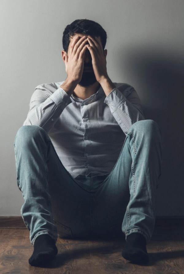 Image of a man sitting on the floor, experiencing muscle aches and sweating during 7 Oh Kratom withdrawal