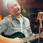 Image of a man playing a guitar in front of a microphone - Country Songs About Sobriety - Ingrained Recovery