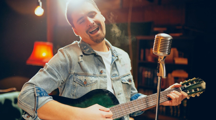 Image of a man playing a guitar in front of a microphone - Country Songs About Sobriety - Ingrained Recovery
