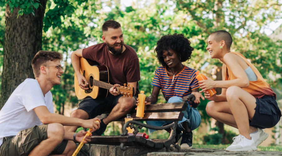 Group of young adult playing guitar in park and hanging out together