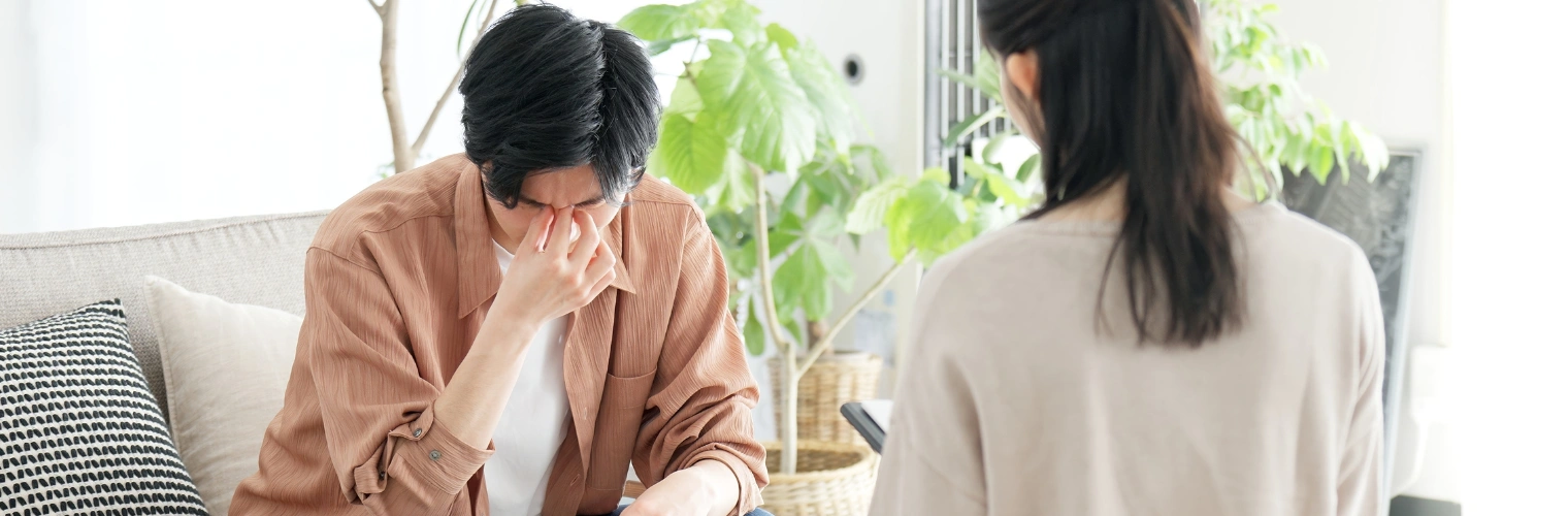 Image of a man sitting in therapy with his hand on his nose as a counselor looks on