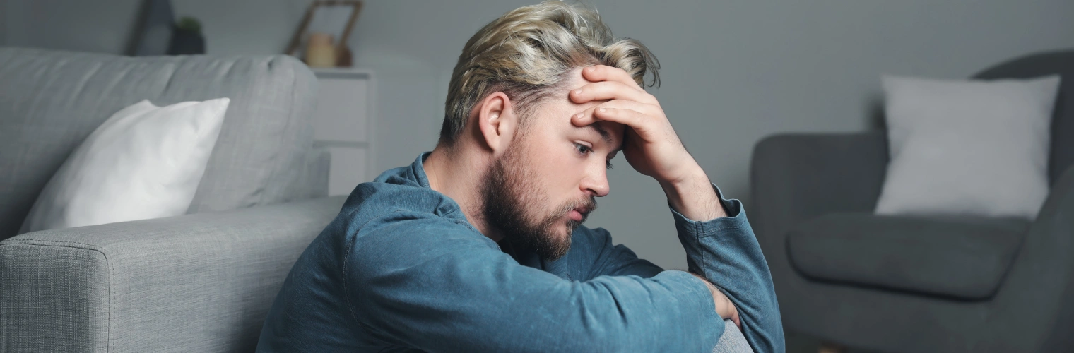 Image of a man sitting on the floor with his hand on his forehead, suffering from substance-Induced Mood Disorders