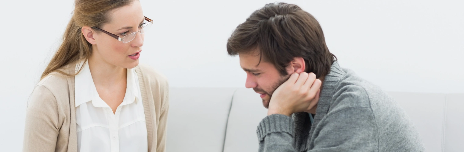 Mixing Meth and Alcohol - Ingrained Recovery Image of a man in pain sitting on a sofa next to a treatment counselor - Mixing Meth and Alcohol - Ingrained Recovery