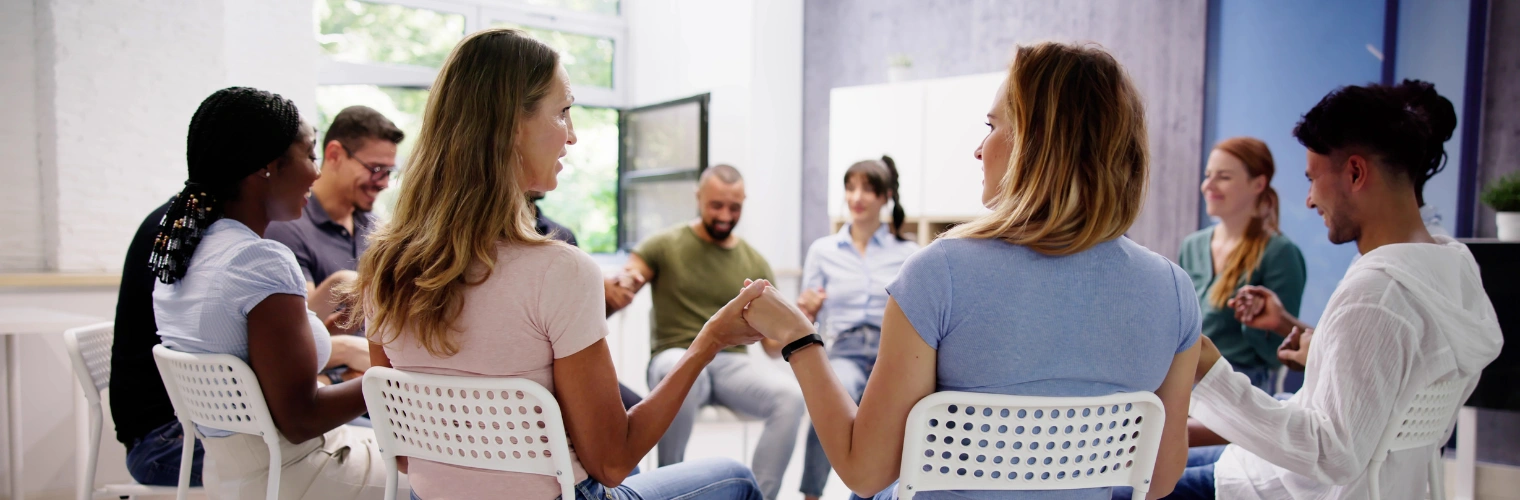 Alcoholics Anonymous Twelve Steps journey with focus on Step Two mage of men and women sitting in a circle and holding each others hands, displaying Alcoholics Anonymous Twelve Steps journey with focus on Step Two