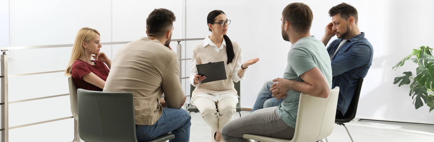 Image of addiction recovery group therapy discussing confidentiality, boundaries, and ethical guidelines with a licensed counselor Image of men and women sitting in an addiction recovery group therapy, discussing confidentiality, boundaries, and ethical guidelines with a licensed counselor