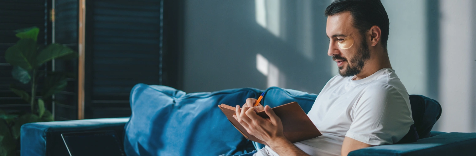 Image of person completing AA fourth step worksheet and exploring root causes of addiction Image of man sitting at home, completing AA fourth step worksheet and exploring root causes of addiction