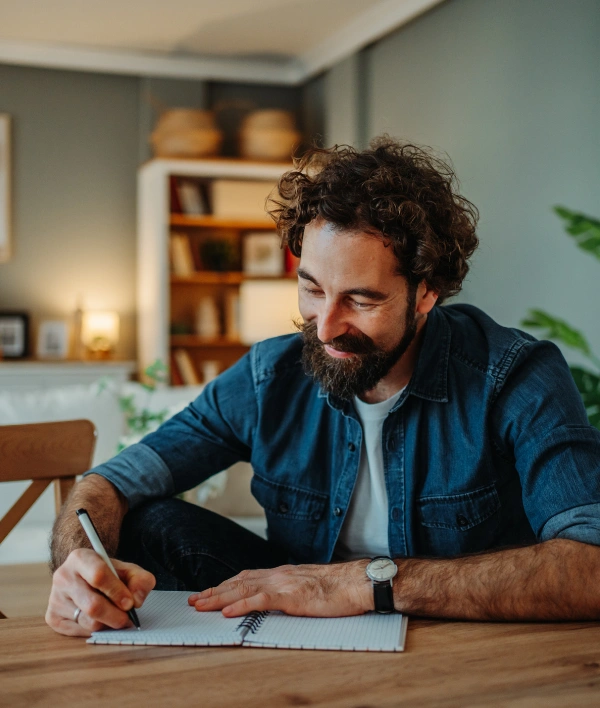 Image of a person writing in a journal at a wooden table Image of a person writing in a journal at a wooden table